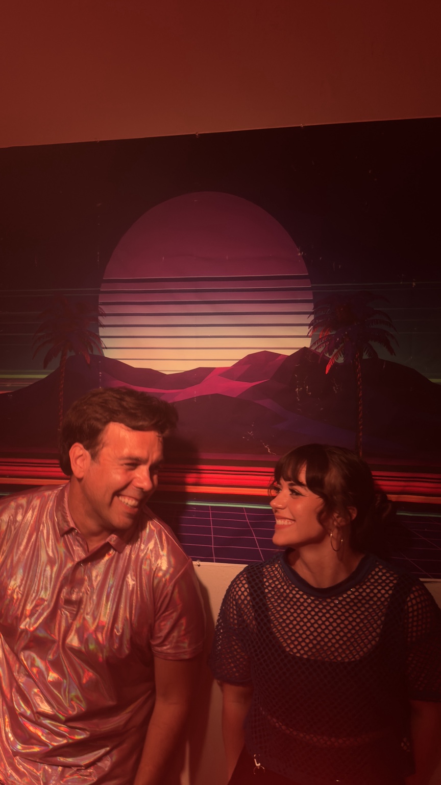 The two members of Songwheels laughing together in a neon setting